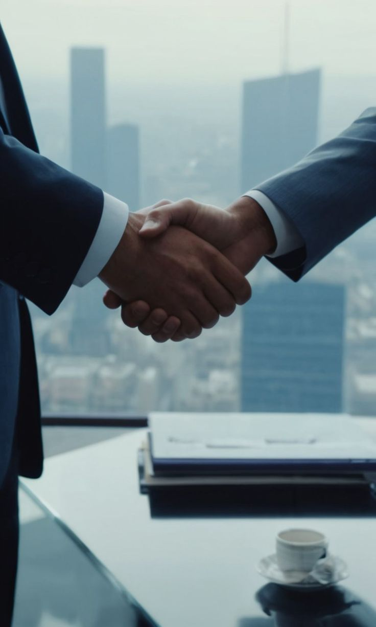 Mãos de duas pessoas em um aperto de mãos em ambiente corporativo.
