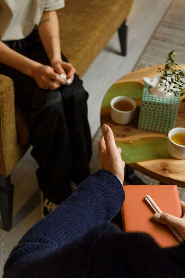 Cena de psicoterapia com duas pessoas em atendimento, poltronas e mesa de apoio.